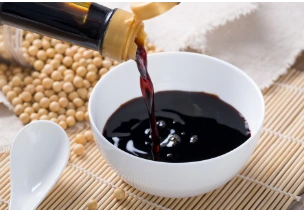 Soy sauce being poured into a white bowl, surrounded by soybeans, highlighting authentic and versatile institutional sauces.