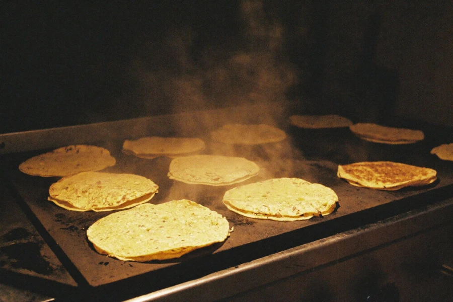 Nixtamalized corn tortillas heating on a commercial grill in a Mexican foodservice kitchen