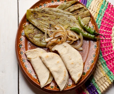 Grilled cactus pads served with onions, peppers, and tortillas